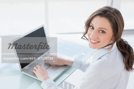 Portrait of a smiling brown haired businesswoman using laptop in a bright office