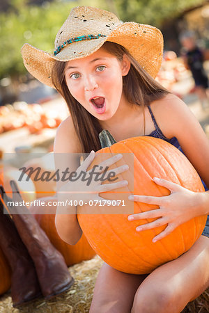 Preteen Girl Holding A Large Pumpkin at the Pumpkin Patch in a Rustic Setting.