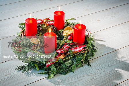 Advent wreath of twigs with four burning red candles and various ornaments