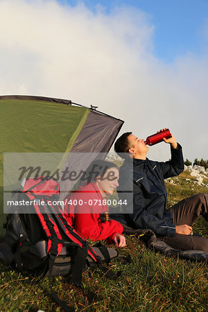 Young couple with a tent is watching the sunset in the mountains