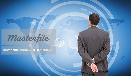 Composite image of businessman standing with hands behind back looking at world map on blue background