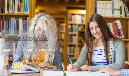 Two female students writing notes at desk in the college library