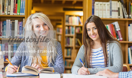 Portrait of two smiling female students writing notes at desk in the college library