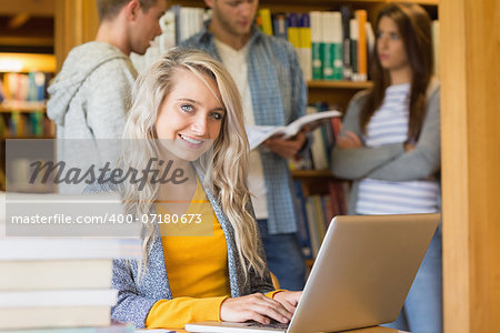 Portrait of a smiling female student using laptop while others in background at the college library