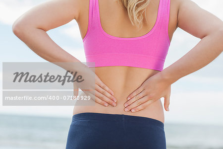 Close up mid section of a healthy woman in sports bra suffering from back pain on beach