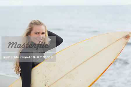 Portrait of a beautiful young woman in wet suit holding surfboard at the beach