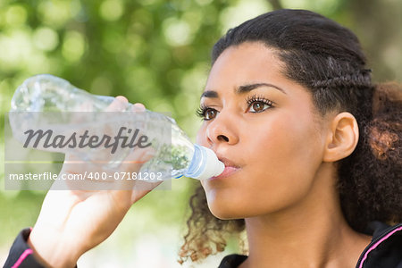 Close up of a tired healthy young woman drinking water in the park