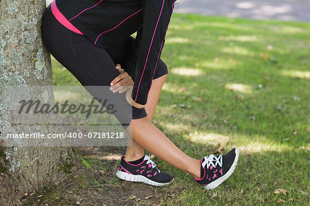 Low section side view of a healthy young woman stretching her leg during exercise at the park