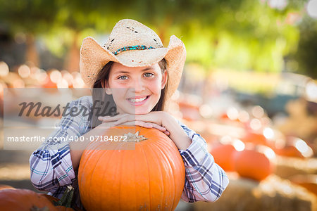Portrait of Preteen Girl Wearing Cowboy Hat Playing at the Pumpkin Patch in a Rustic Country Setting.