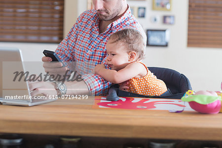 Man working at kitchen counter with baby sitting beside