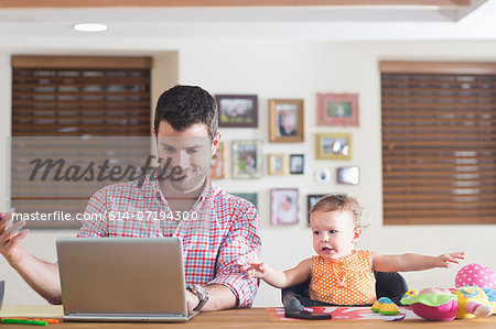 Man working at kitchen counter with baby sitting beside Man working at kitchen counter with baby sitting beside