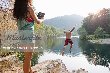 Woman photographing boyfriend jumping from rock ledge, Hamburg, Pennsylvania, USA Woman photographing boyfriend jumping from rock ledge, Hamburg, Pennsylvania, USA