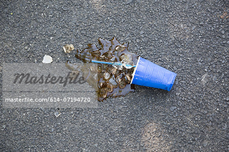 Spilled soft drink with plastic cup and ice cubes on tarmac