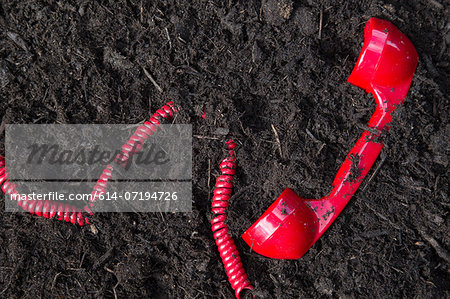 Red retro telephone handset buried in soil