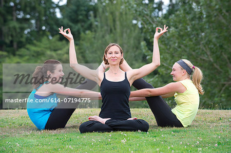 Teenage girls and yoga tutor sitting on grass