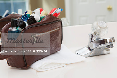 Men's toiletry travel bag on bathroom counter, filled with toothbrush, lotion, razor and other grooming products, USA