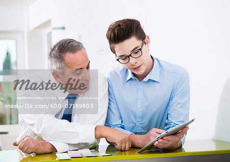 Businessman and apprentice looking at talet computer in office, Germany