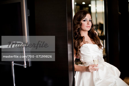 Portrait of young woman in wedding gown, holding glass of champagne and looking at camera, Ontario, Canada