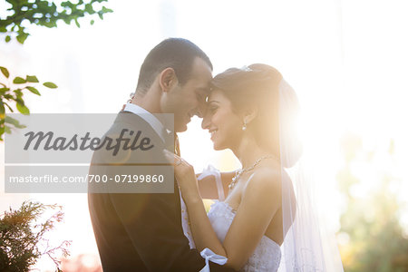 Close-up portrait of bride and groom standing outdoors, face to face, smiling and embracing, Ontario, Canada