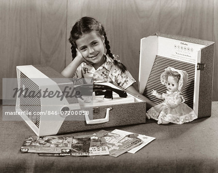 1950s SMILING GIRL LISTENING TO PORTABLE RECORD PLAYER LOOKING AT CAMERA