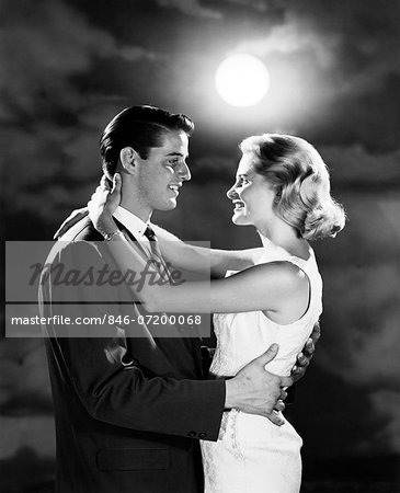 1960s YOUNG COUPLE EMBRACING IN MOONLIGHT