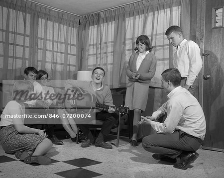 1950s 1960s GROUP OF YOUNG TEENAGERS GATHERING AROUND BOY PLAYING GUITAR