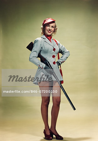 1940s 1950s PORTRAIT SMILING BLOND WOMAN PINUP WEARING HUNTING OUTFIT HOLDING SHOTGUN LOOKING AT CAMERA