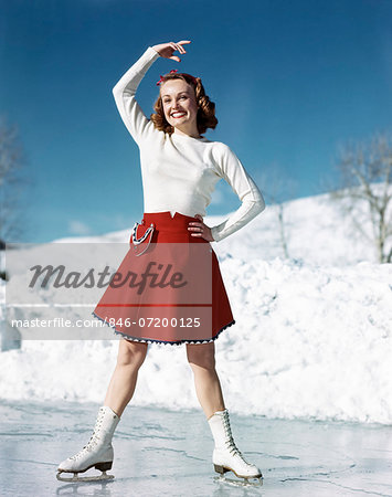 1950s SMILING WOMAN WEARING WHITE SWEATER RED SKIRT ICE SKATING POSING WITH ARM OVER HEAD