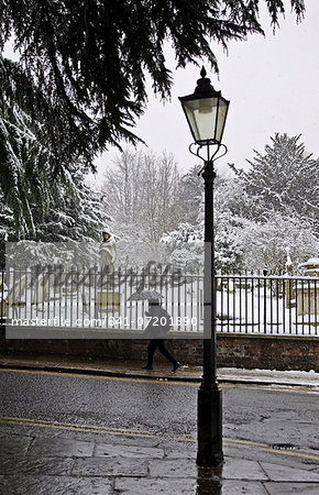 Woman with umbrella walks past snow covered graveyard, Hampstead, North London, United Kingdom
