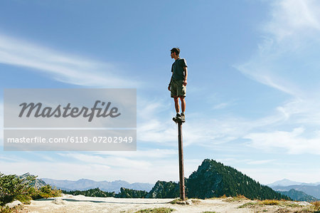 A man standing and balancing on a metal post, looking towards expansive sky, on Surprise Mountain, Alpine Lakes Wilderness, Mt. Baker-Snoqualmie national forest.