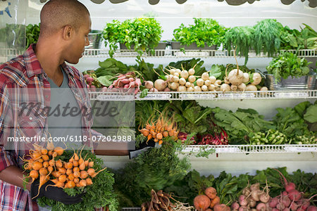 A farm stand with rows of freshly picked vegetables for sale. A man holding bunches of carrots.