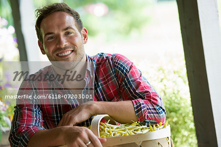 A farm stand with fresh organic vegetables and fruit. A man holding a full basket of beans. A farm stand with fresh organic vegetables and fruit. A man holding a full basket of beans.