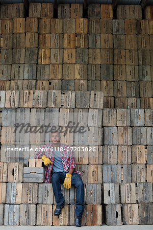 A farmyard. A stack of traditional wooden crates for packing fruit and vegetables. A man sitting on a packing case.
