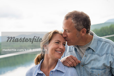 A mature couple standing by a lake shore.