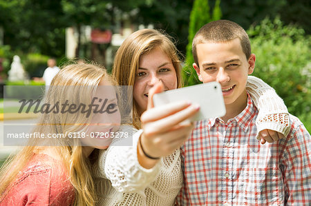 Three young people, two girls and a boy, posing and taking selfy photographs.