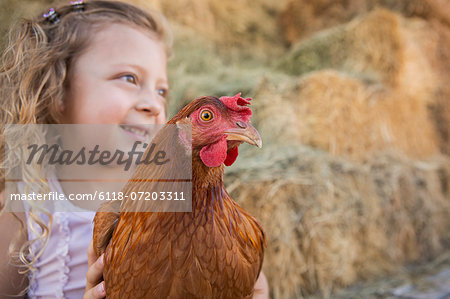 A young girl holding a chicken in a henhouse.