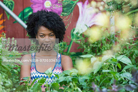 A woman standing in a plant nursery, surrounded by plants, flowers and foliage.