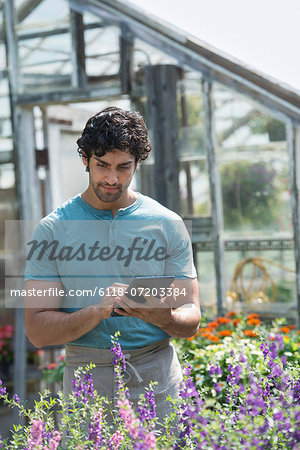 A young man working in a plant nursery, surrounded by flowering plants.