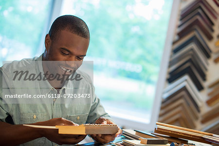 A young man at his workbench in a picture framing studio. Surrounded by samples.