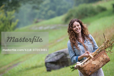A young woman carrying a basket of freshly harvested garlic and vegetables.