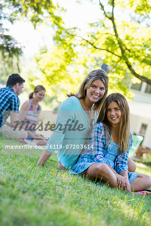 A group of adults and children sitting on the grass under the shade of a tree. A family party.