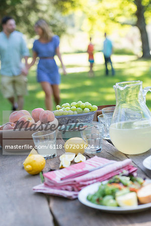 A summer buffet of fruits and vegetables, laid out on a table. People in the background.