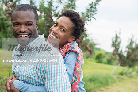 An organic apple tree orchard. A couple hugging and smiling at the camera.