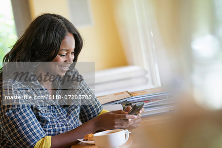 A woman seated at a table with a cup of coffee, using a smart phone.