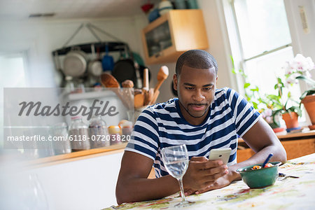 A man sitting at a table using a smart phone. Fruit dessert and a glass of wine at hand.