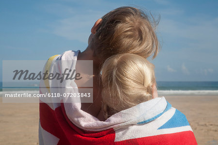 Two children sharing a towel. Back view of a brother and sister sitting on the beach looking out to sea.