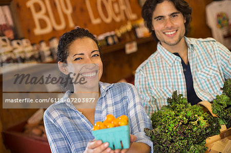 Two people with baskets of tomatoes and curly green leafy vegetables. Working on an organic farm.