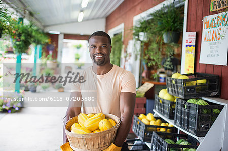 Working on an organic farm. A man carrying a large basket of yellow squash vegetables. Displays of fresh produce for sale.