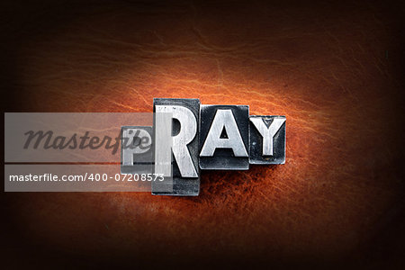 The word pray made from vintage lead letterpress type on a leather background.