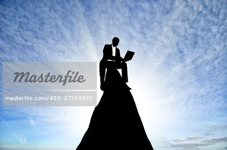 silhouette of a businessman with a laptop in hand is on top of a mountain in the sky with clouds.